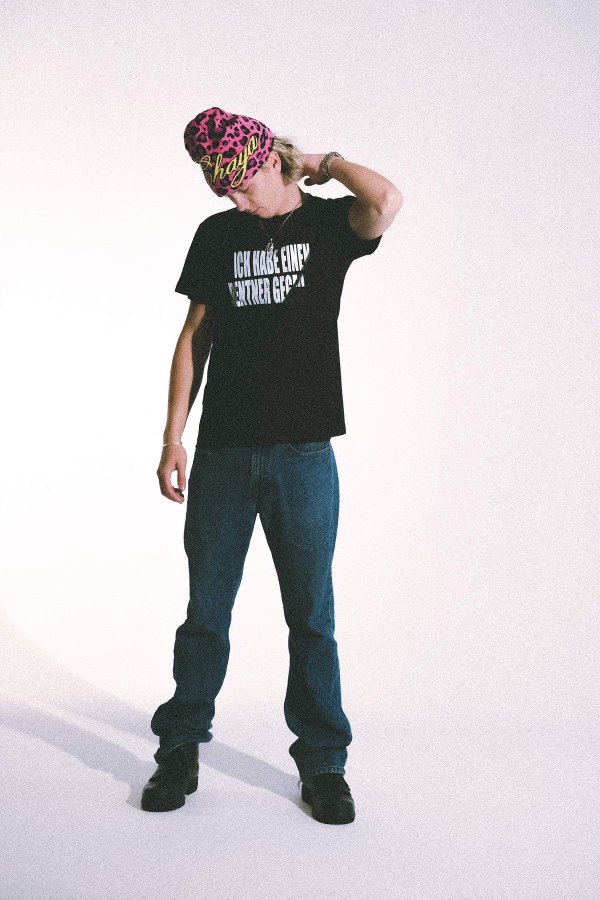 Noah Kraus mit pinker Leo-Beanie trägt schwarzes T-Shirt mit weißem Textprint „ICH HABE EINEN …“ und Jeans, Studio