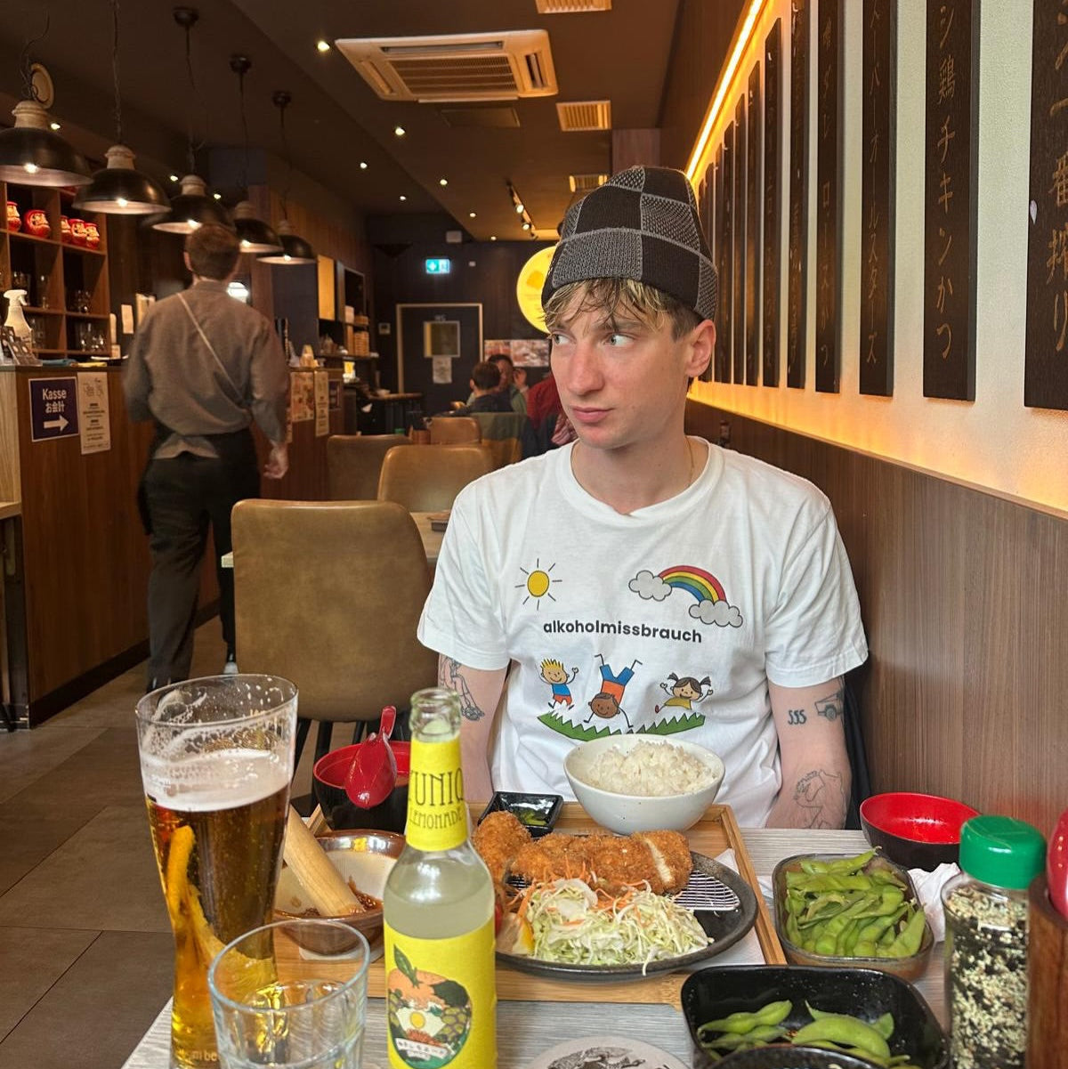 Model trägt weißes „alkoholmissbrauch" T-Shirt mit kindlichem Frontprint beim Essen in einem japanischen Restaurant, großes